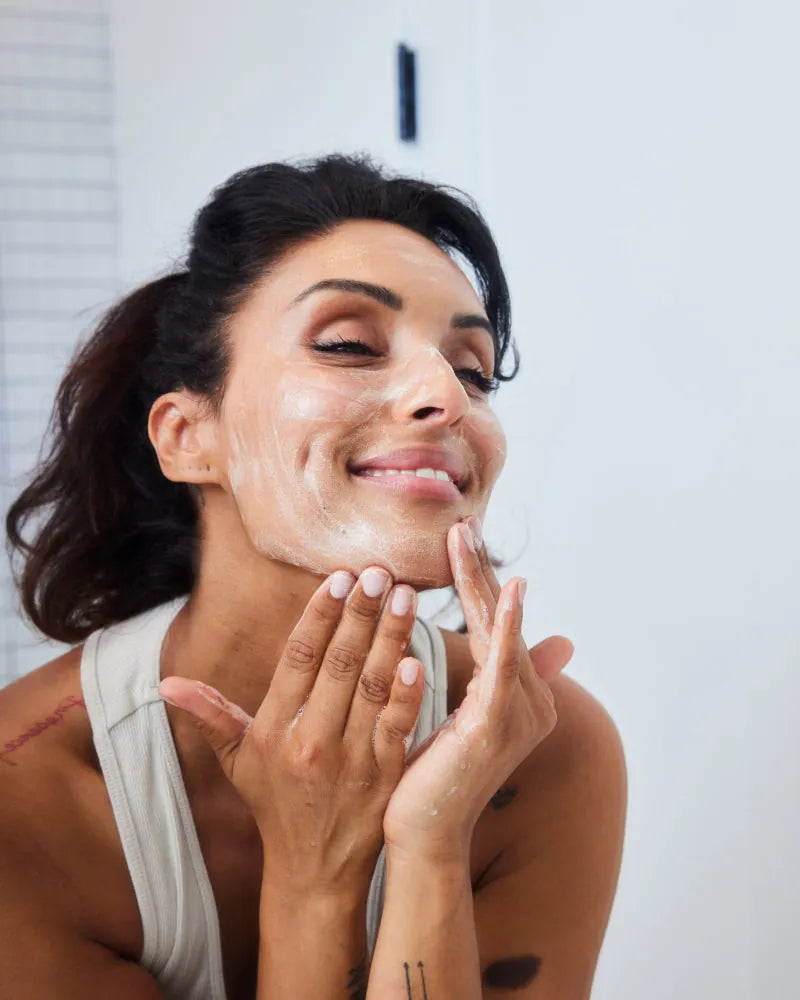 Woman applying Bio-Cleanse 5.5 Face wash lather to her face, smiling w