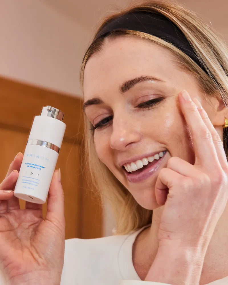 Happy woman gently touching eye area while holding Regenerative ECM Ey