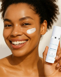 Smiling woman with radiant skin applying Clear Fusion Sunscreen with visible product on cheek gallery position 1