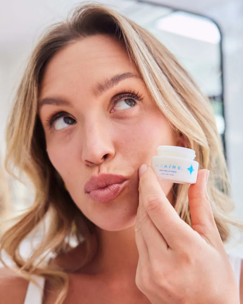 Woman holding Peptide Lip Mask jar close to face with a playful expres